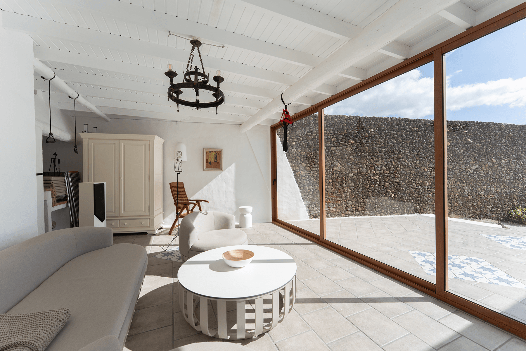 Salón acristalado con techo de vigas blancas y salida a patio de piedra en villa Lanzarote